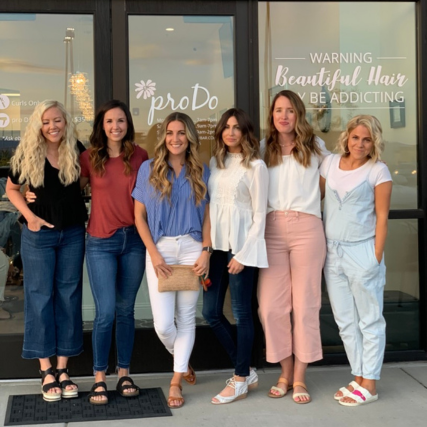 Six women standing together outside Pro Do Blow Dry Bar, celebrating together in front of the salon storefront.