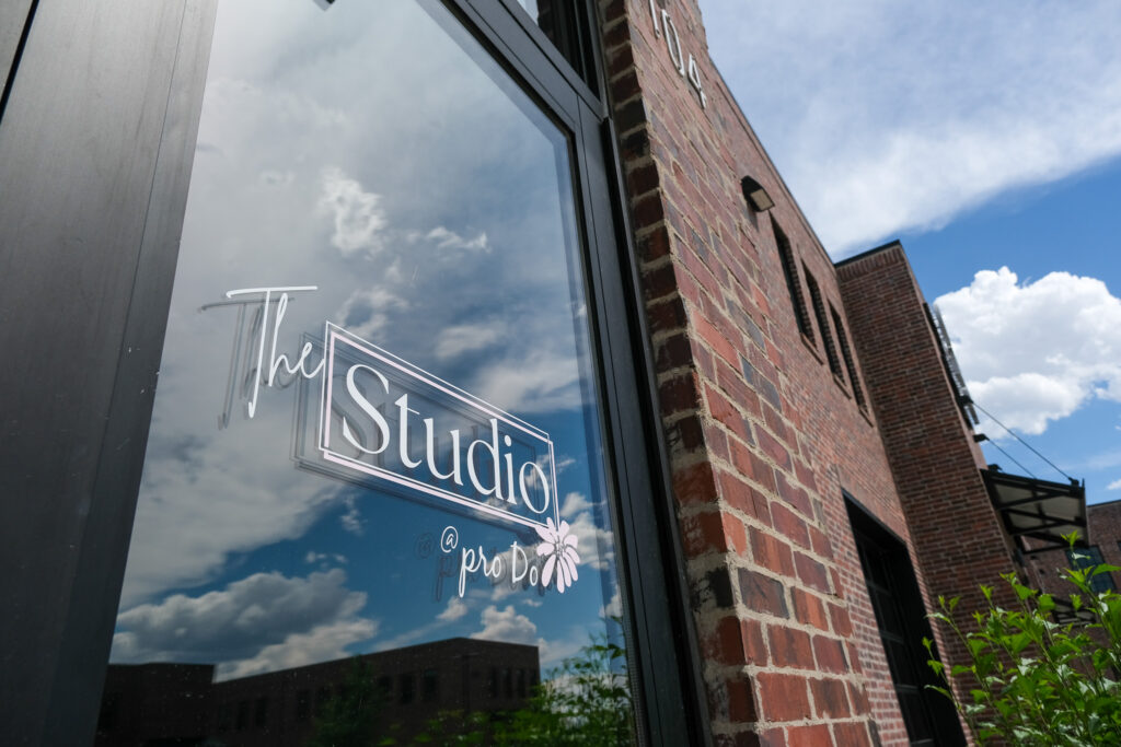The Studio at pro Do Blow Dry Bar entrance window with the Studio logo and cloudy sky reflection