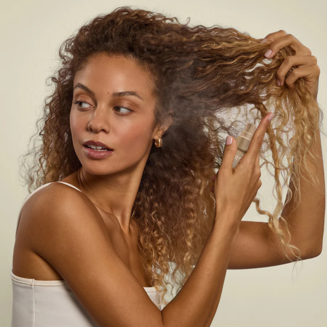 Woman spraying Kitsch hair perfume onto long curly hair
