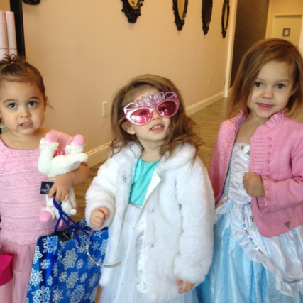 Three young girls wearing princess-inspired outfits in pink and blue, with one girl wearing oversized pink sunglasses and a white faux-fur coat.