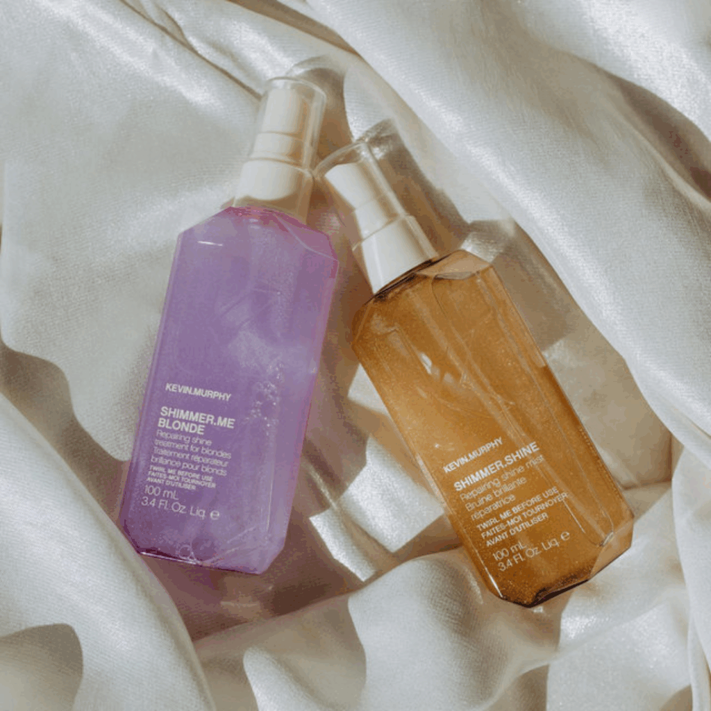 Kevin Murphy Shimmer Shine and Shimmer Me Blonde lightweight shine sprays displayed on soft fabric, used to add glossy finish and enhance blonde and brunette hair during professional blowouts at Pro Do Blow Dry Bar.