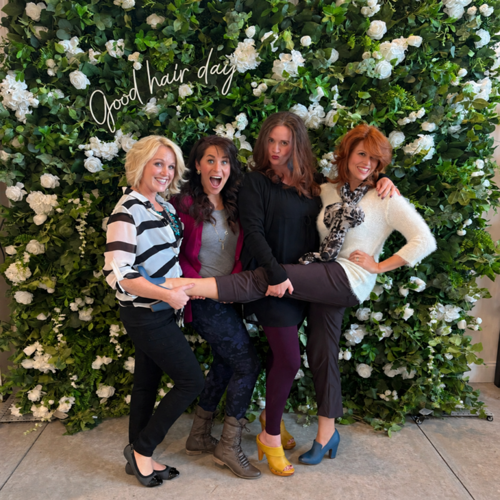 Four friends at The Ready Room flower wall with a softly lit Good hair day sign