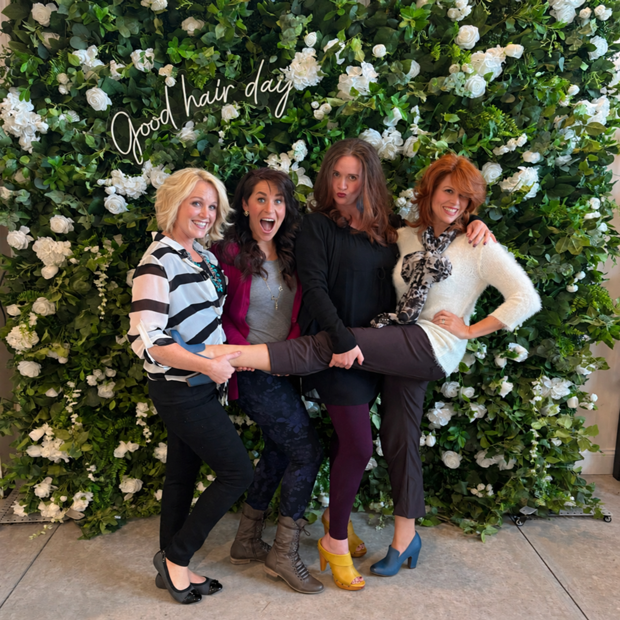 Four friends at The Ready Room flower wall with a softly lit Good hair day sign