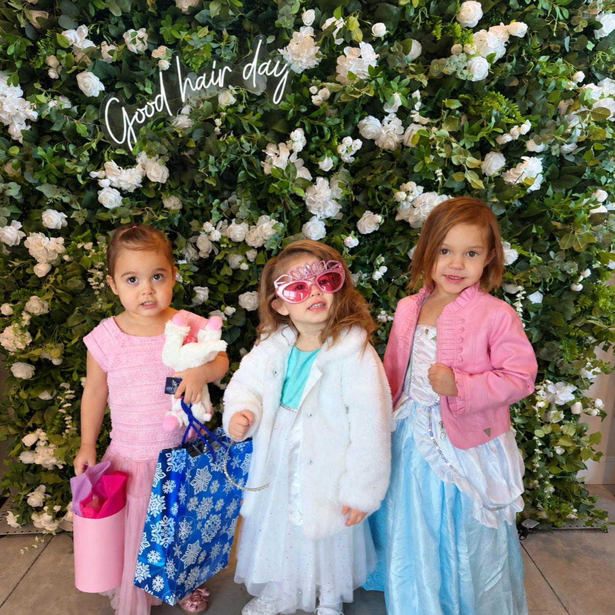 Three girls dressed up in front of the flower wall and softly glowing Good hair day sign at The Ready Room